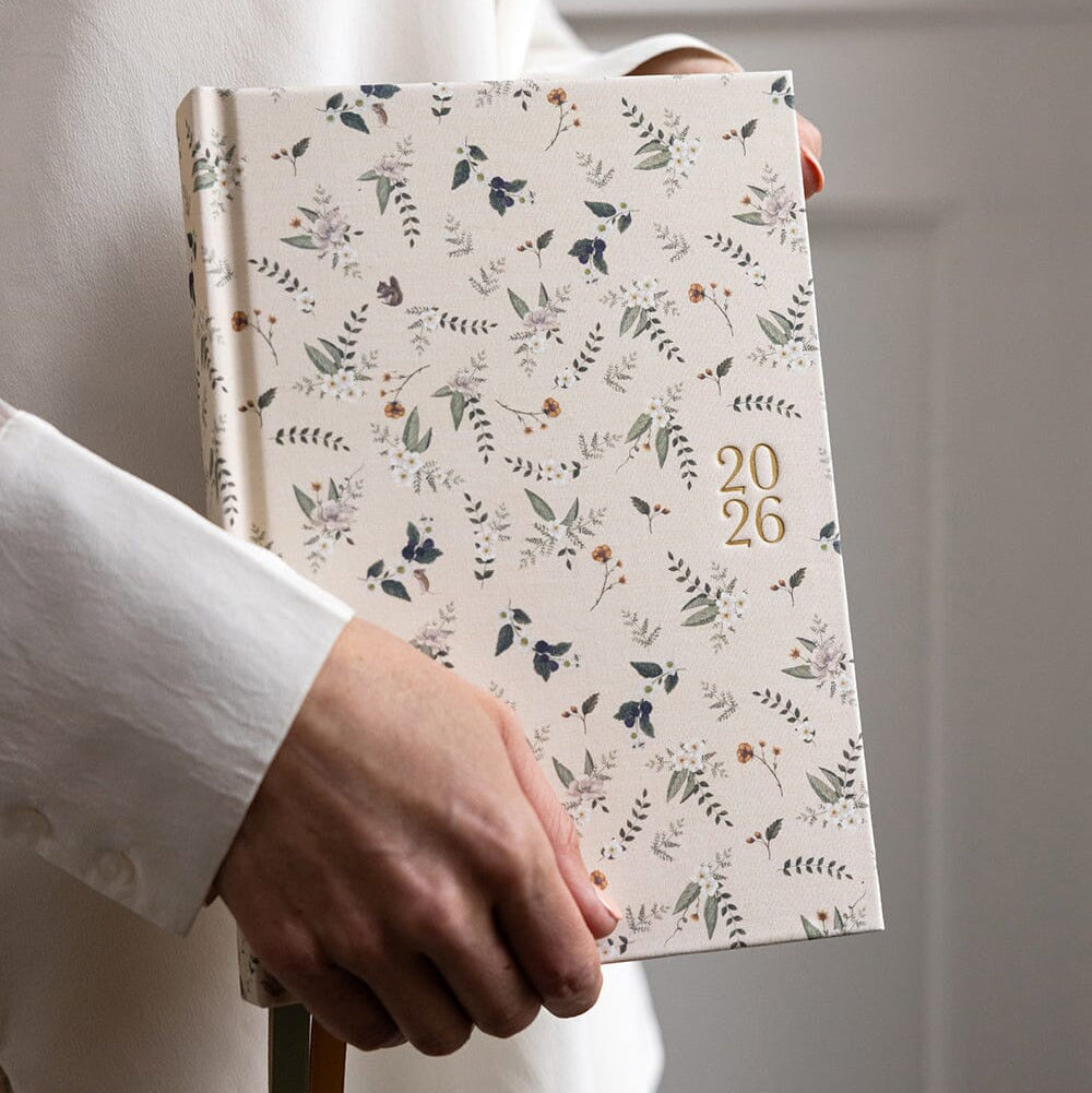 Person holding a floral-patterned notebook with '2026' on a plain background