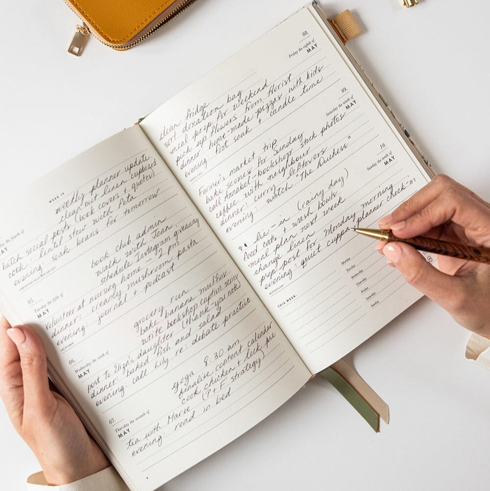 Person writing in a notebook with a pen on a white surface
