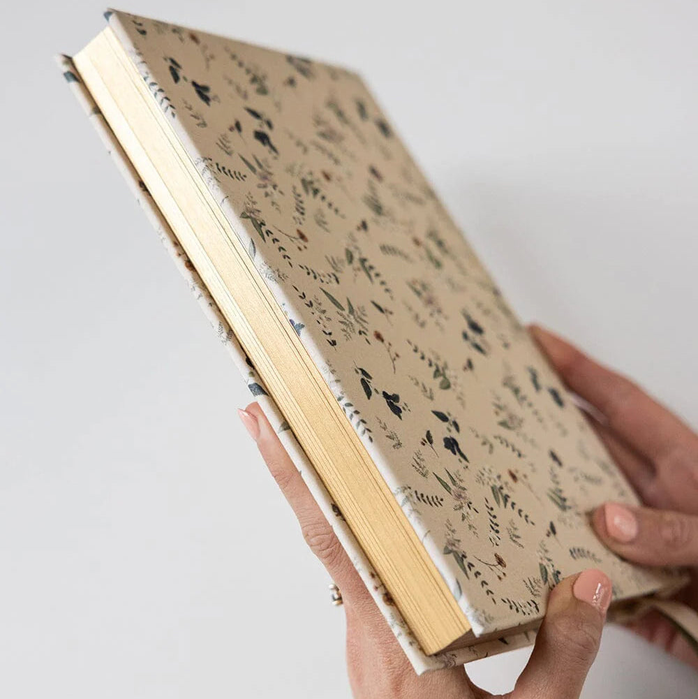 Hand holding a notebook with a floral pattern on a light gray background
