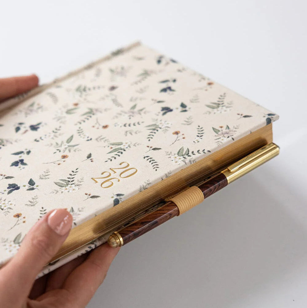 Hand holding a floral notebook with a pen holder on a white background