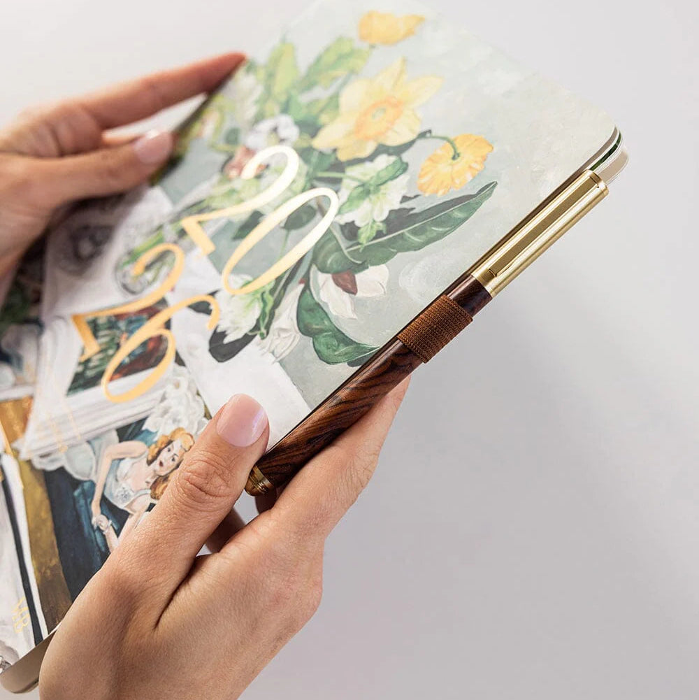 Hand holding a decorative pen over a notebook with floral design