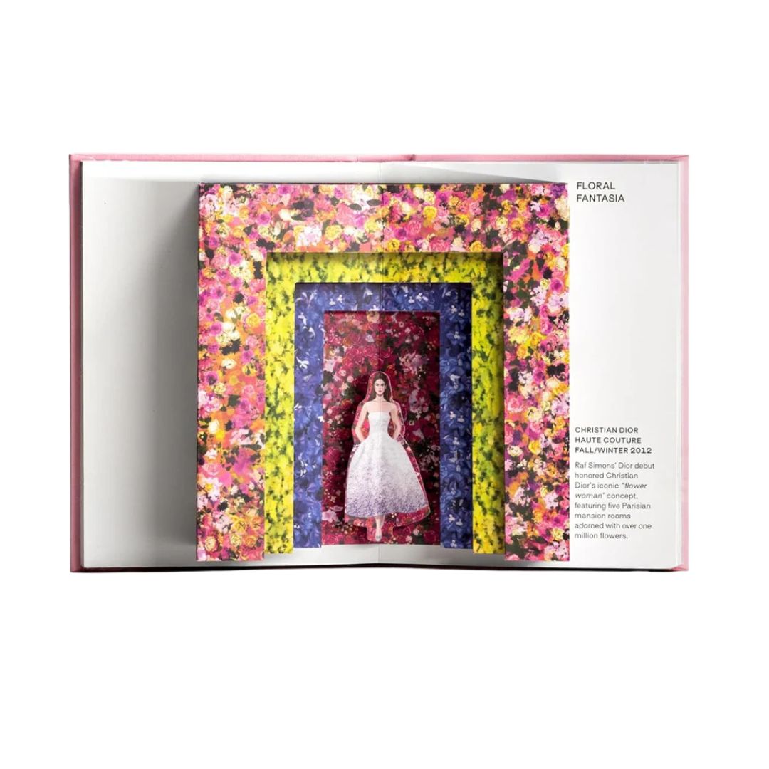 Open book displaying a colorful floral frame with a dress inside, on a white background.