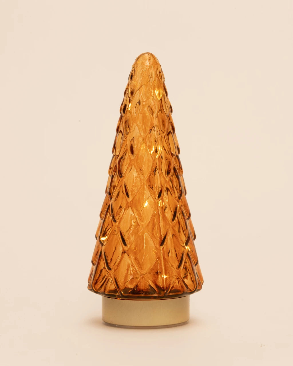 An amber glass Christmas tree-shaped decorative light or lamp with a textured, diamond-patterned surface and a gold-toned circular base, set against a plain off-white background.