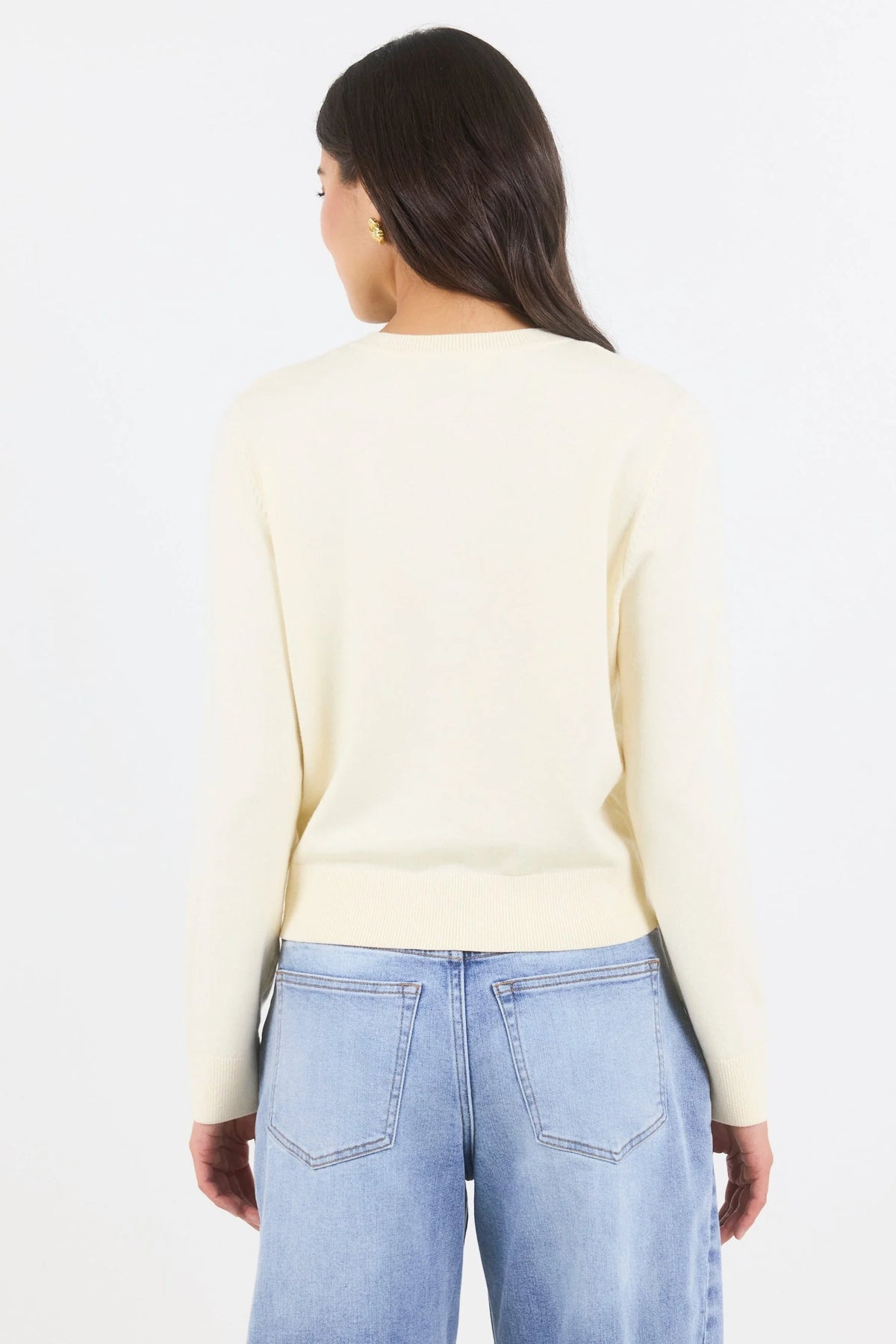 Person wearing a light yellow sweater and blue jeans on a white background