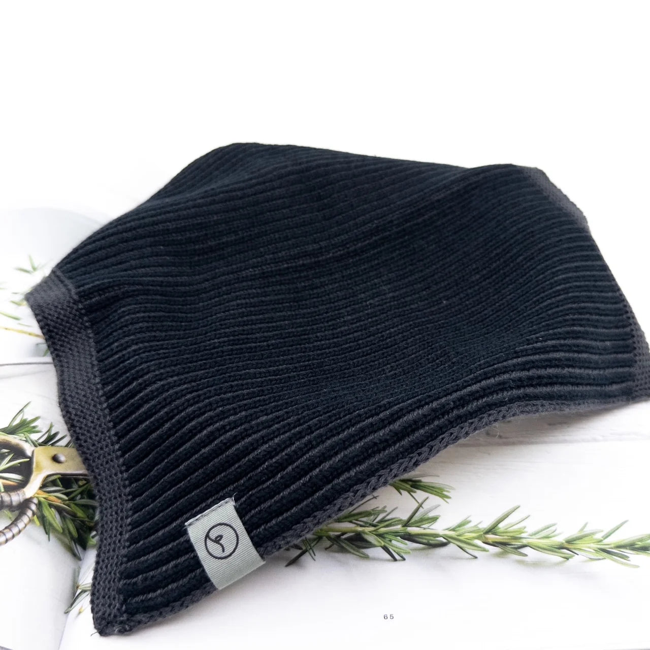 Black knit beanie with a brand tag on a white background with greenery