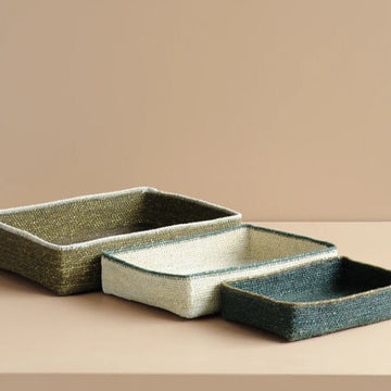 Set of three rectangular woven trays on a beige surface with a beige background