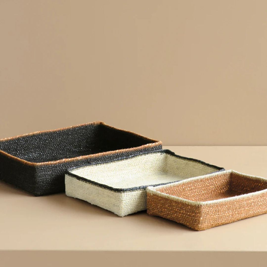 Three woven trays in black, white, and brown on a beige surface with a beige background