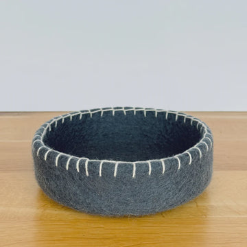 Gray felted bowl with white stitching on a wooden surface
