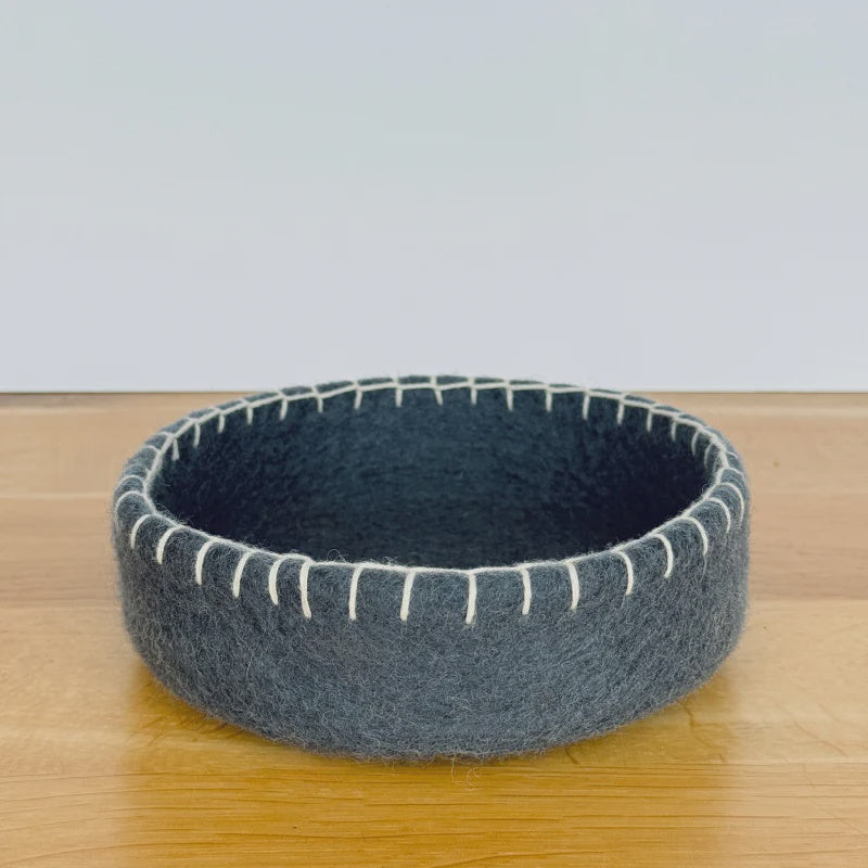 Gray felted bowl with white stitching on a wooden surface