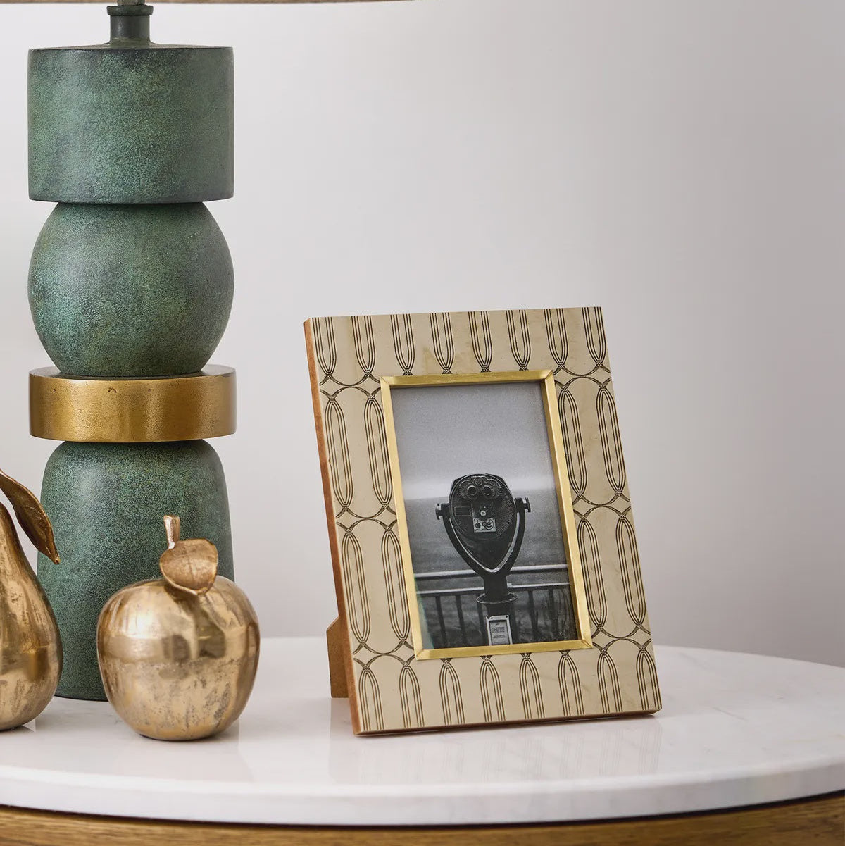 Decorative table with a green lamp, gold ornaments, and a photo frame on a white surface.