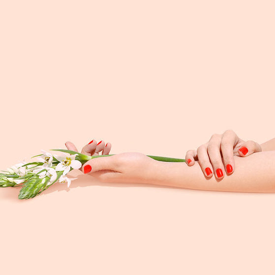 Two hands with red nail polish holding a small bouquet of flowers on a beige background