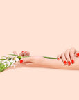 Two hands with red nail polish holding a small bouquet of flowers on a beige background