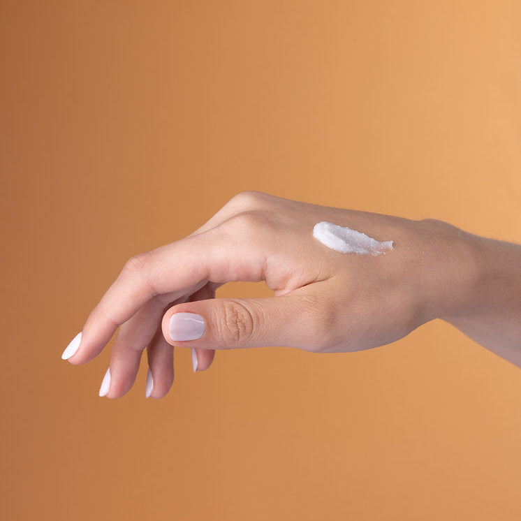 Hand applying cream on a brown background