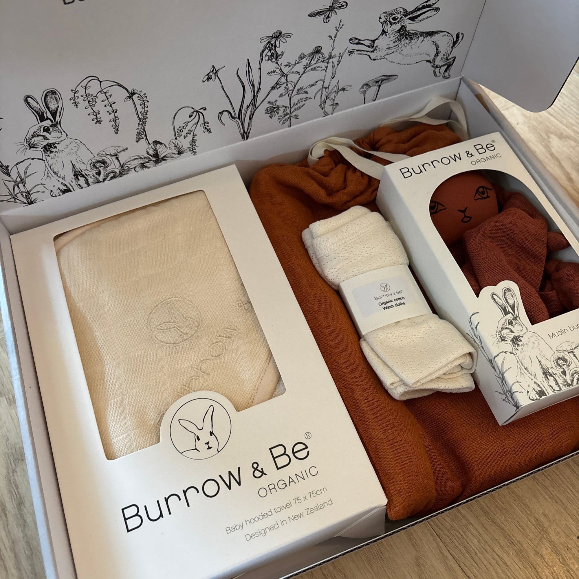 Baby clothing and accessories in a 'Bunrow & Be' box on a wooden surface