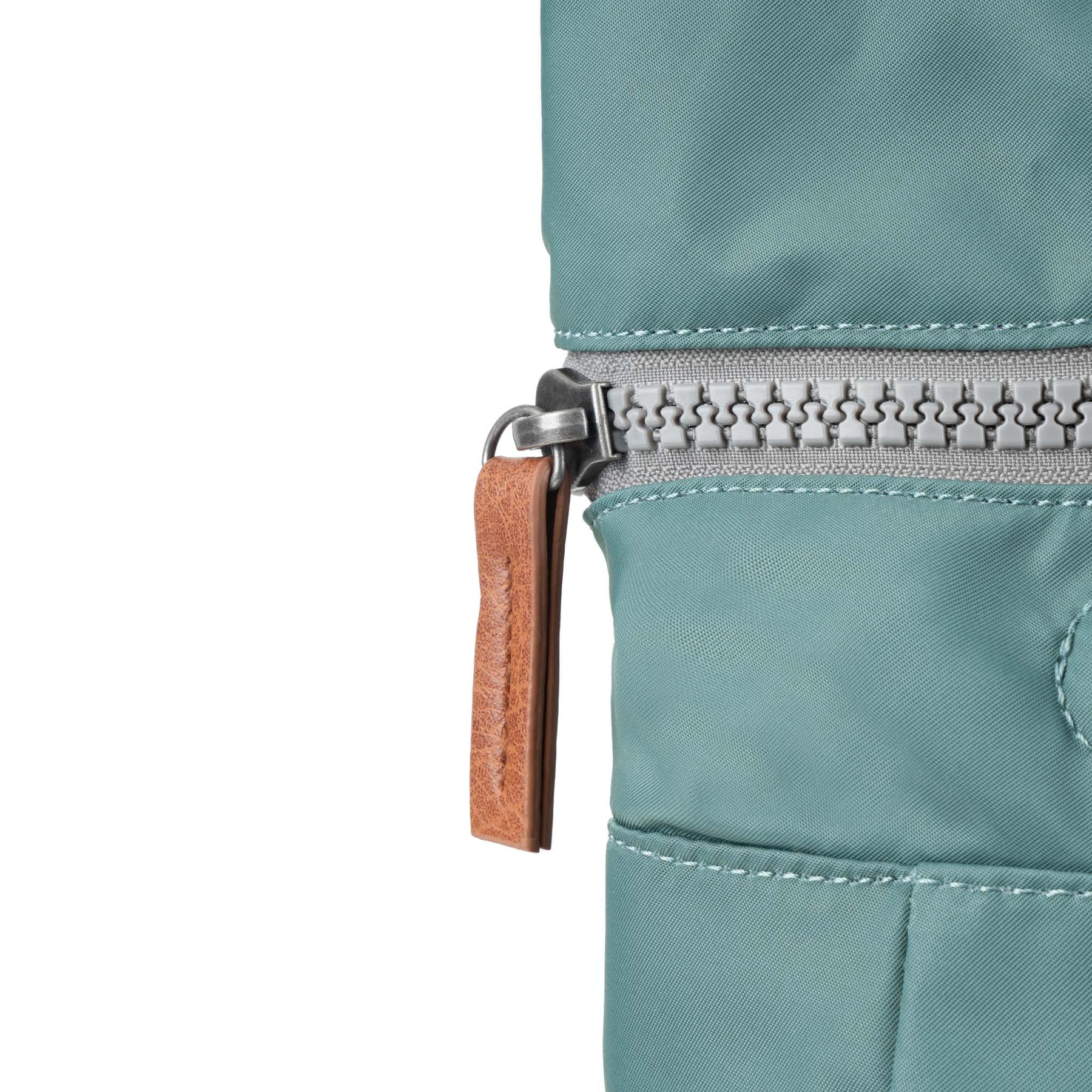 Close-up of a teal jacket with a zipper and brown pull tab on a white background