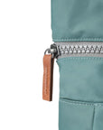 Close-up of a teal jacket with a zipper and brown pull tab on a white background