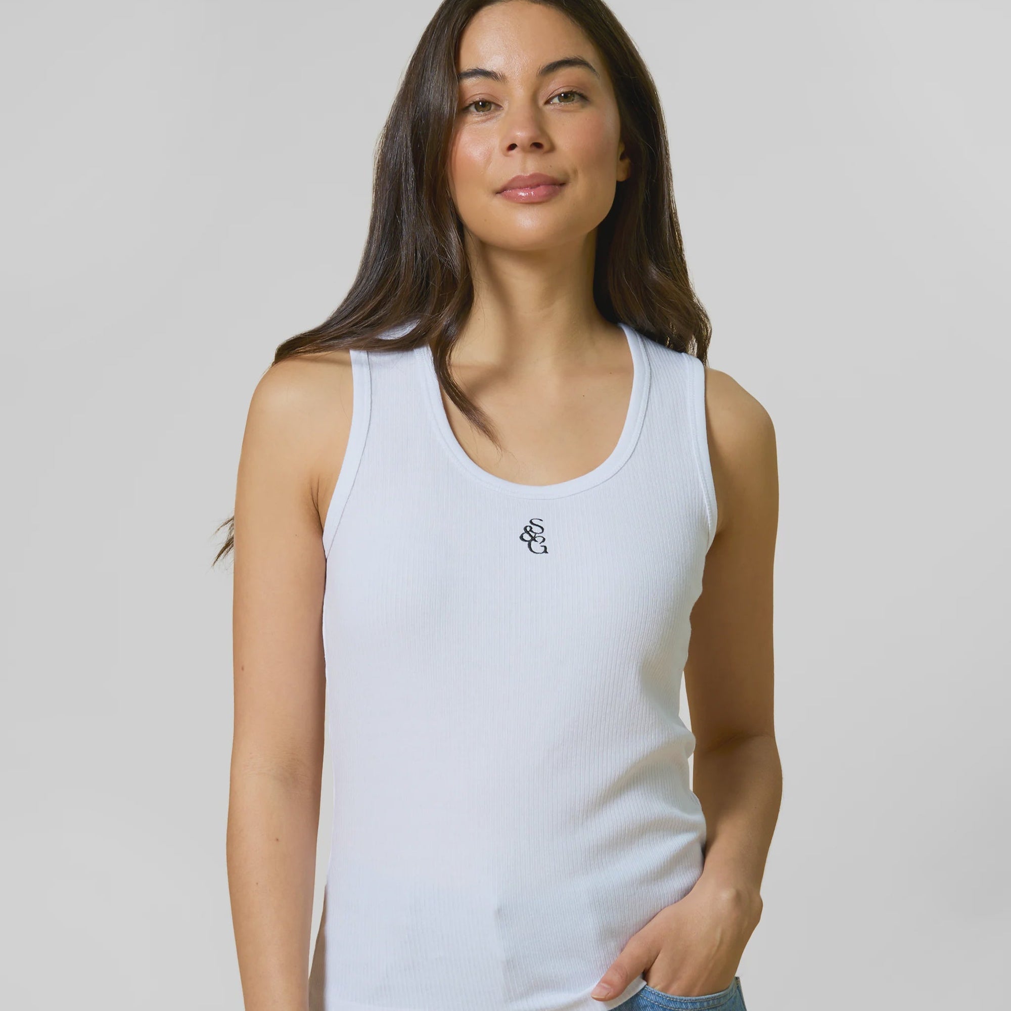 Woman wearing a white tank top with a small logo on a plain background