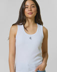 Woman wearing a white tank top with a small logo on a plain background
