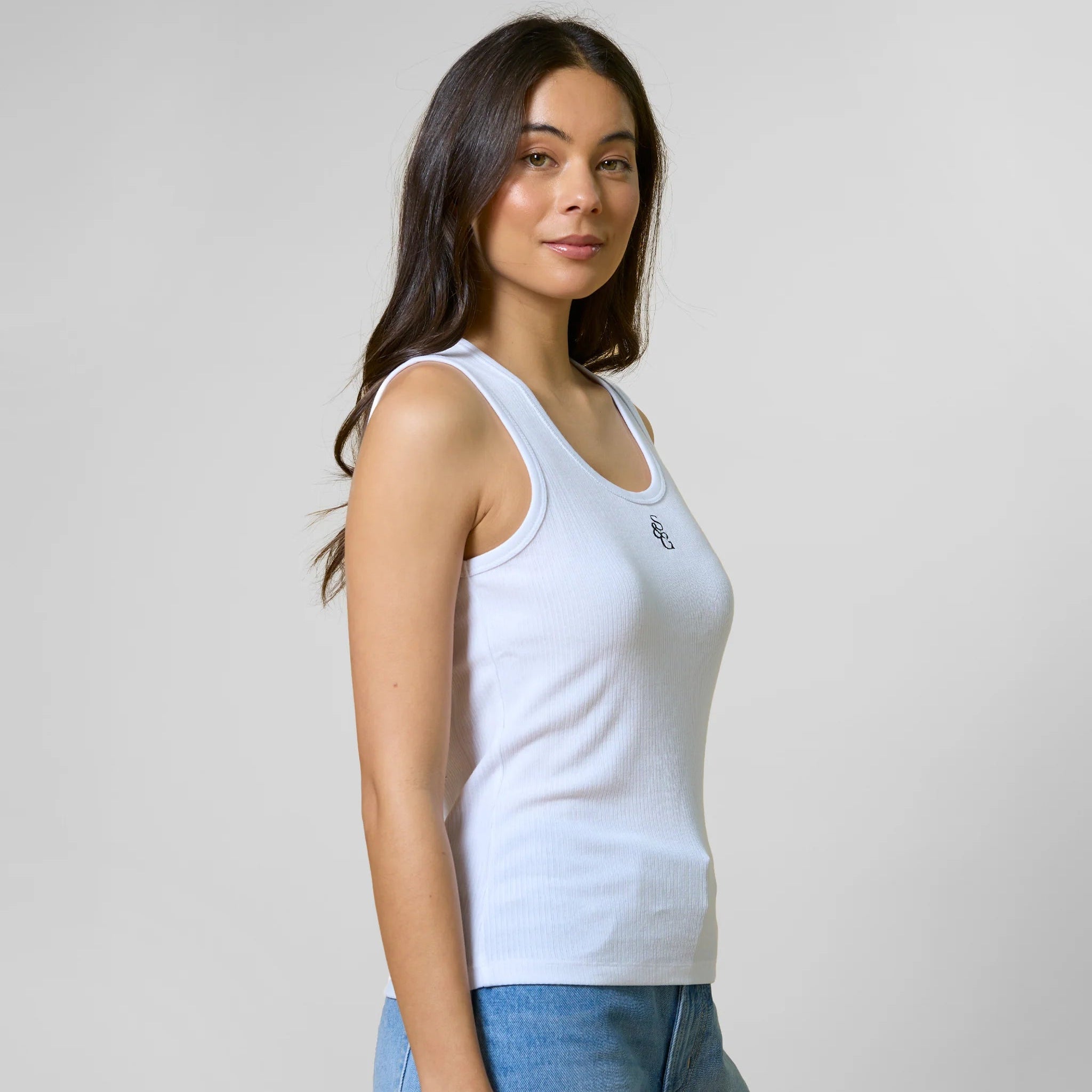 Woman wearing a light blue tank top and jeans against a plain background