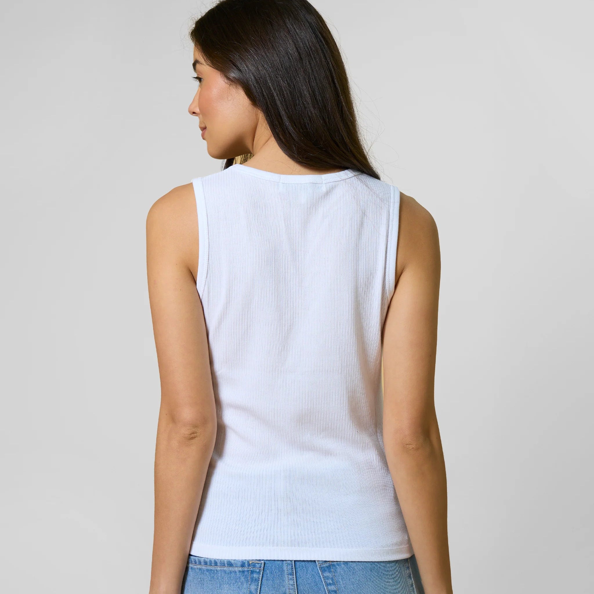 Woman wearing a white sleeveless top and blue jeans against a plain background