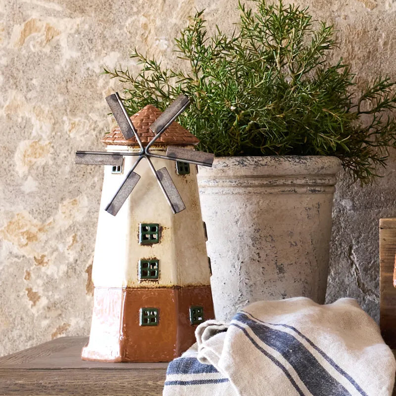 Decorative windmill and potted plant on a wooden surface with a stone wall background