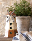 Decorative windmill and potted plant on a wooden surface with a stone wall background