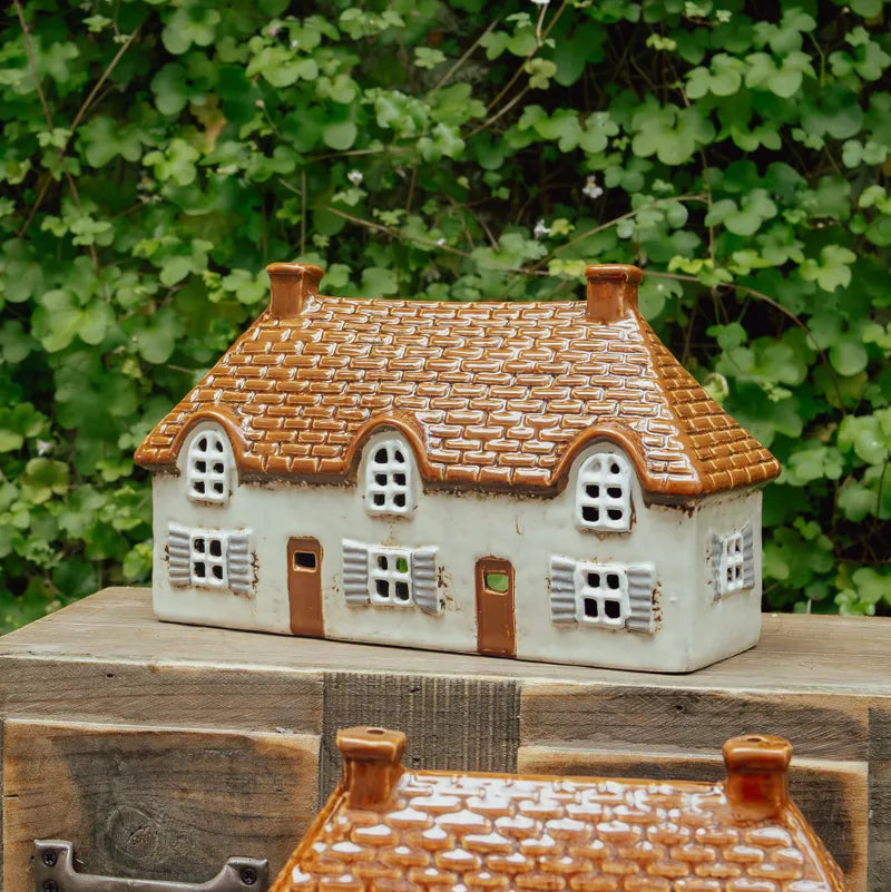 Ceramic house figurine with a thatched roof on a wooden surface with green foliage in the background