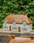 Ceramic house figurine with a thatched roof on a wooden surface with green foliage in the background
