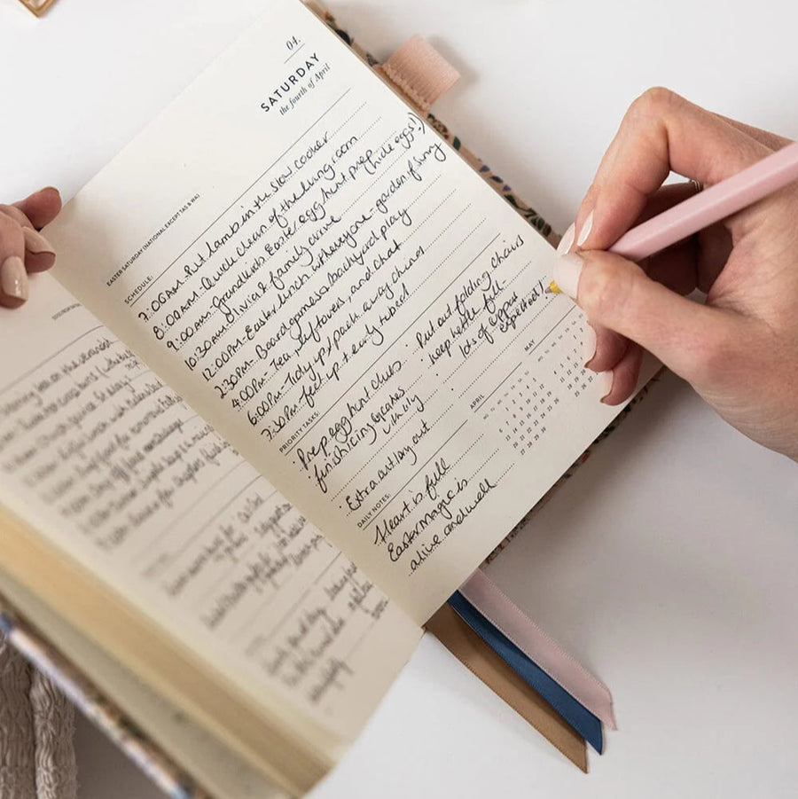 Person writing in a notebook with a pink pen on a white surface
