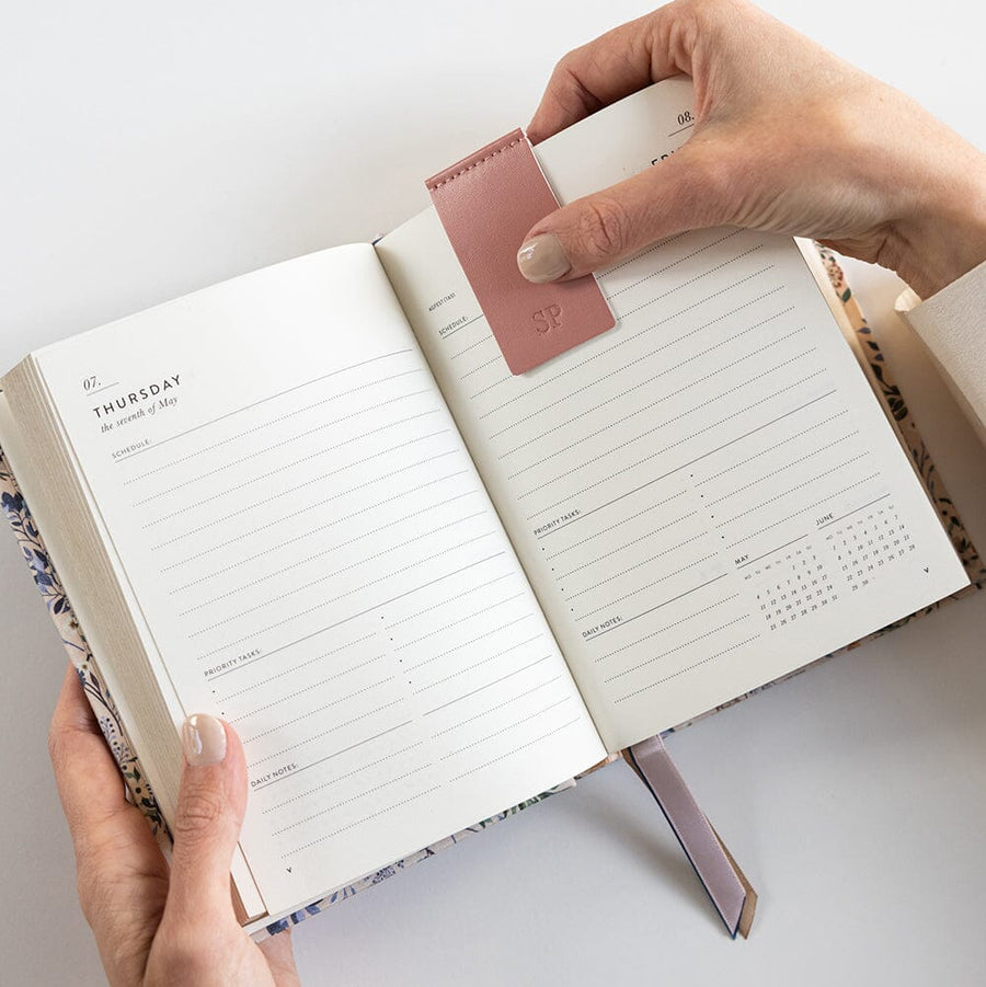 Person holding an open planner with a pink leather cover on a light gray background