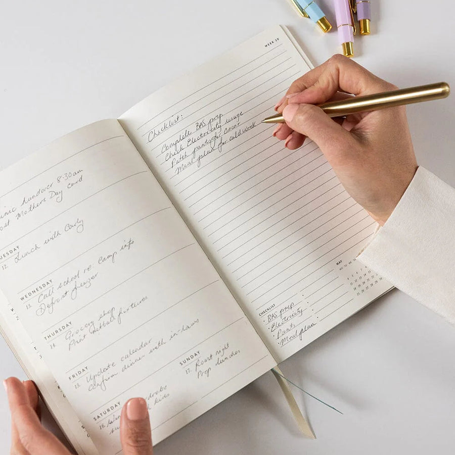 Person writing in a notebook with a gold pen on a light surface.