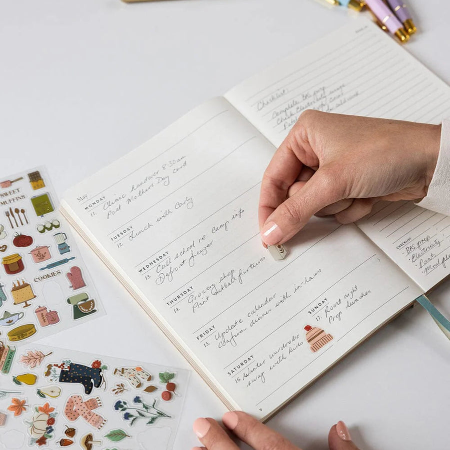 Handwritten notes in a notebook with decorative stickers and pens on a light surface