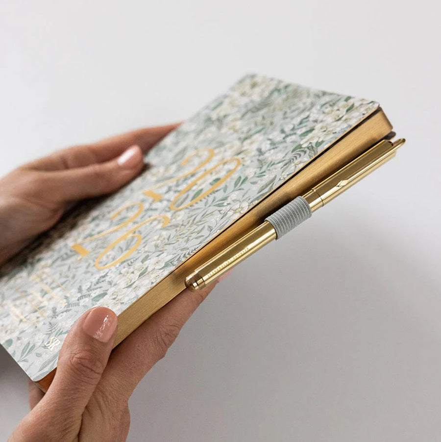 Hand holding a floral notebook with a gold edge on a light gray background