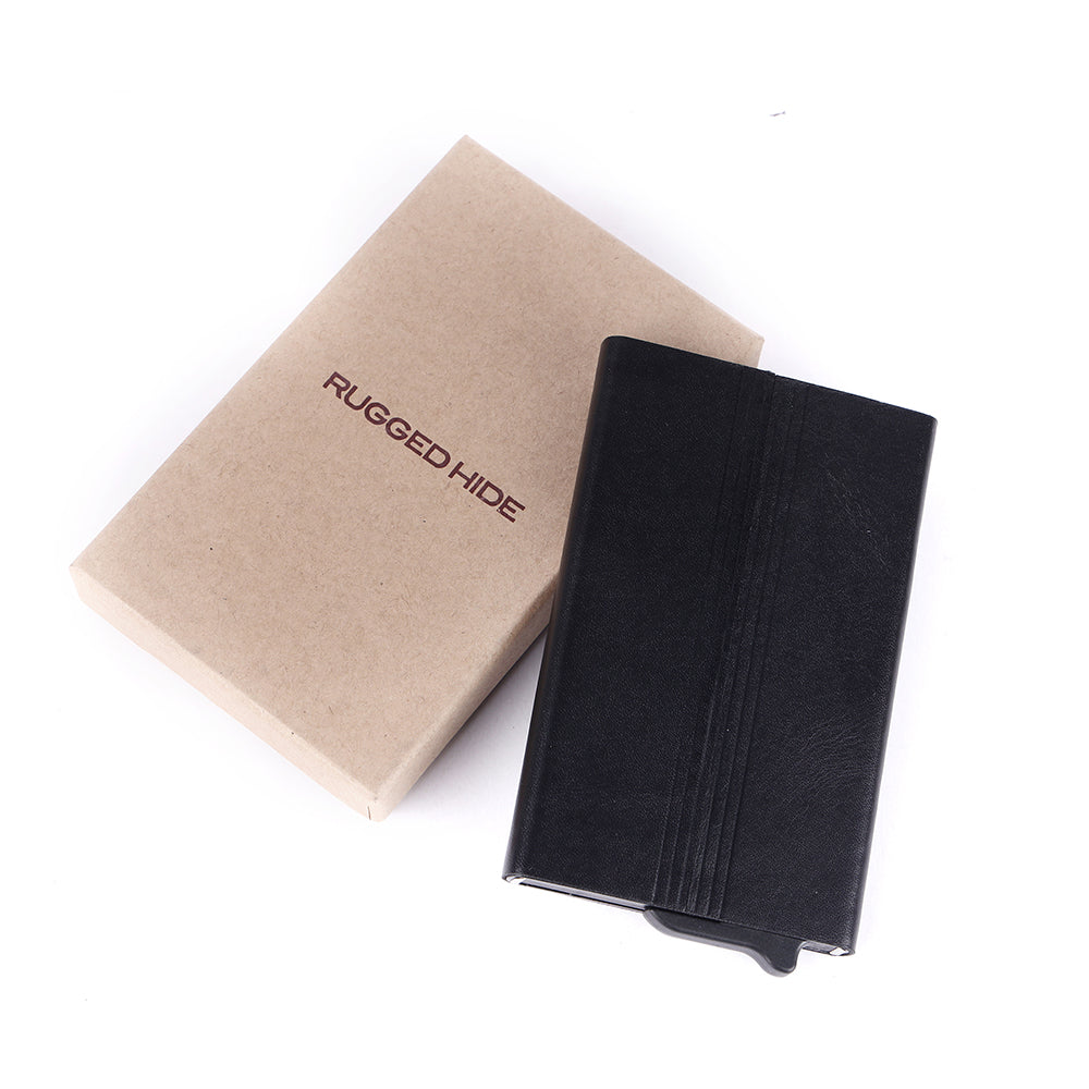 A black textured leather wallet or card holder shown next to its kraft paper packaging box, which is printed with the brand name 'RUGGED HIDE'.