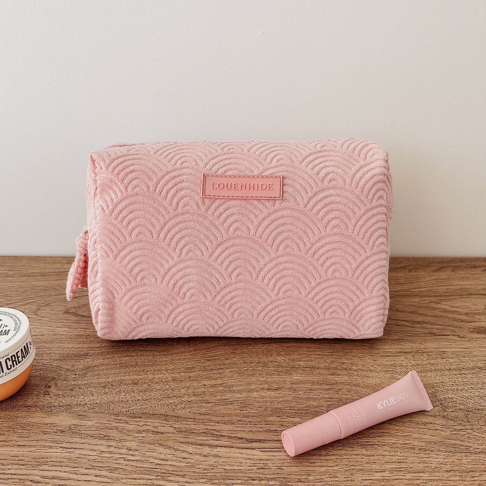 Pink textured pouch with a brand logo on a wooden surface