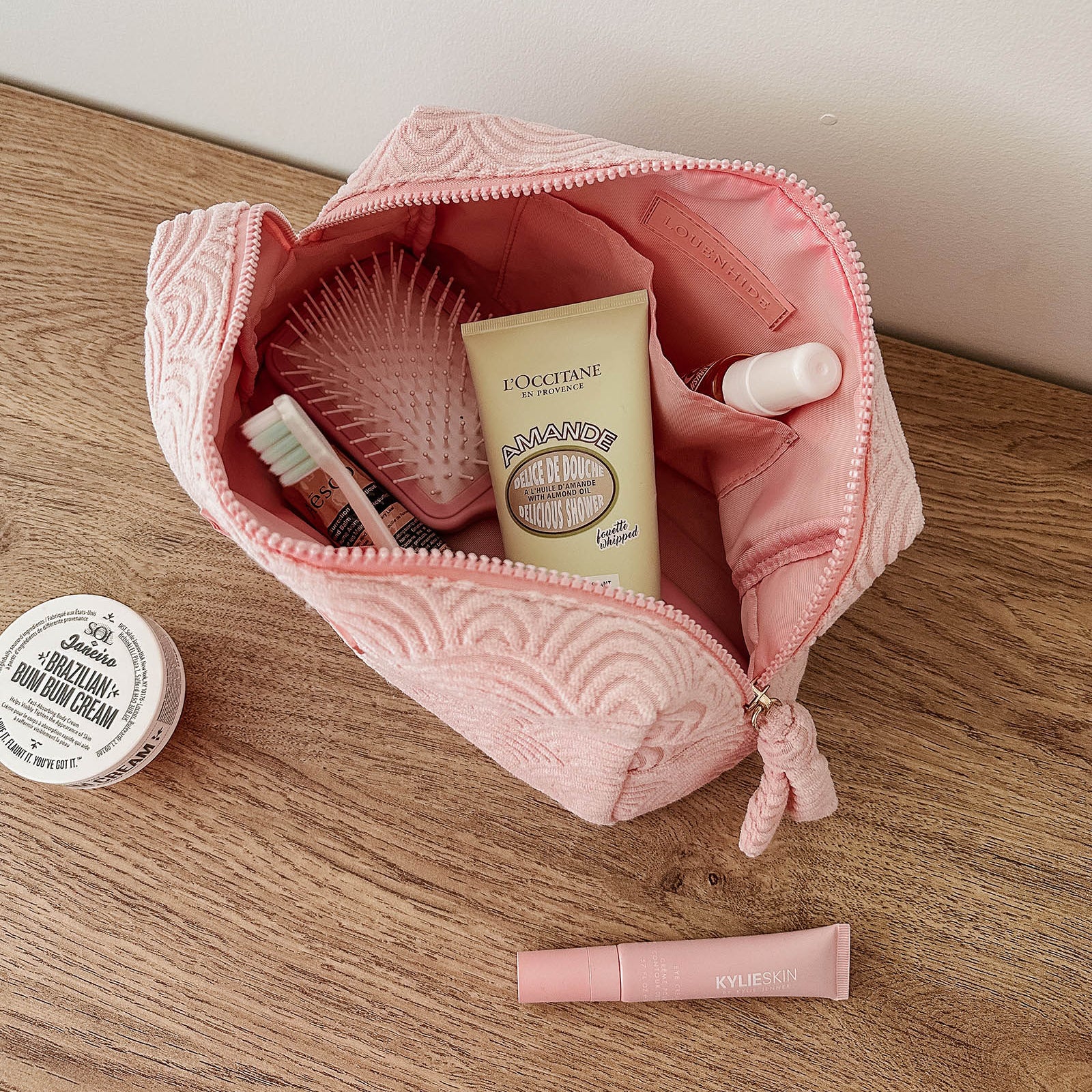Pink toiletry bag with cosmetic items on a wooden surface