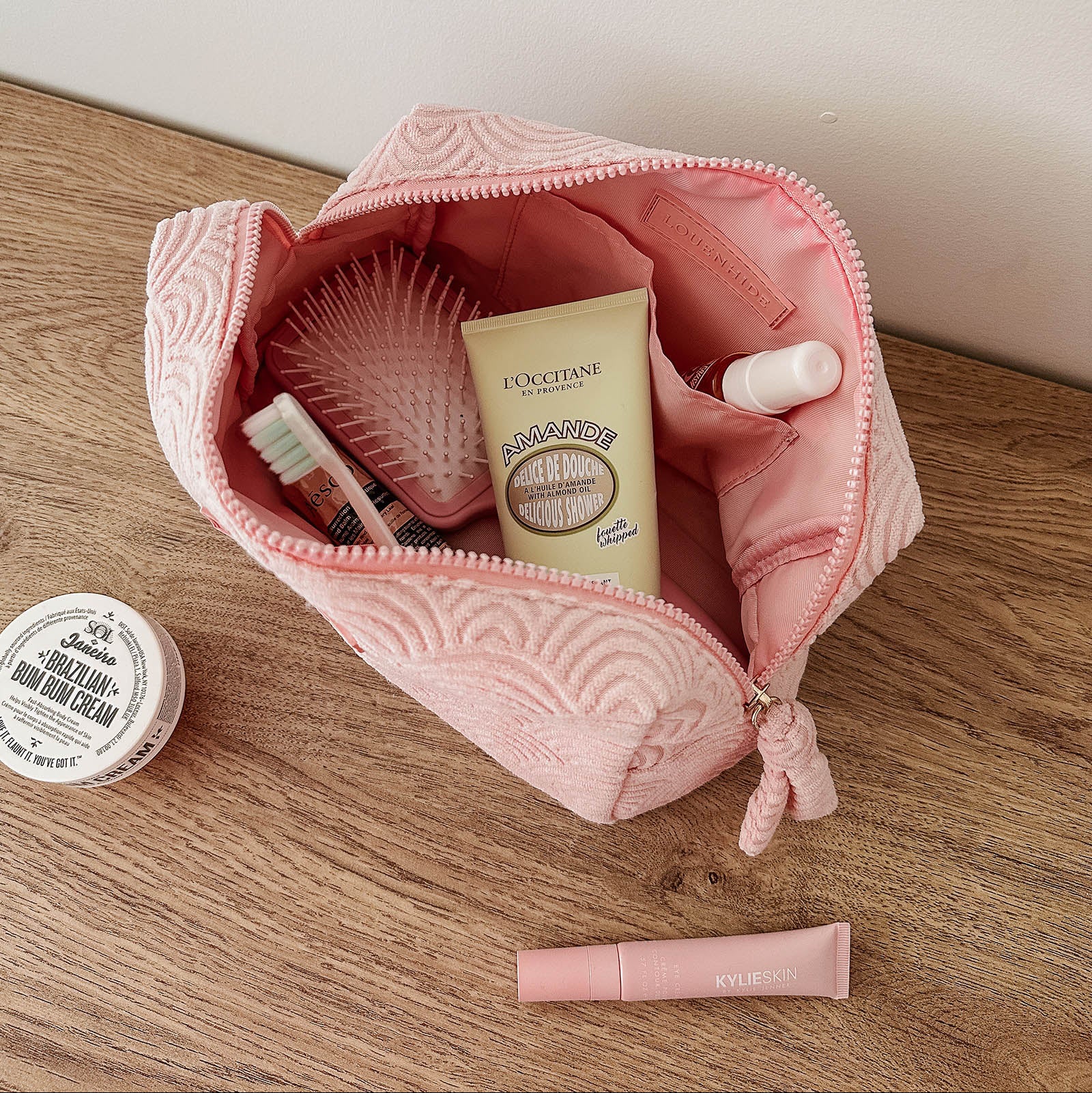 Pink toiletry bag with cosmetic items on a wooden surface