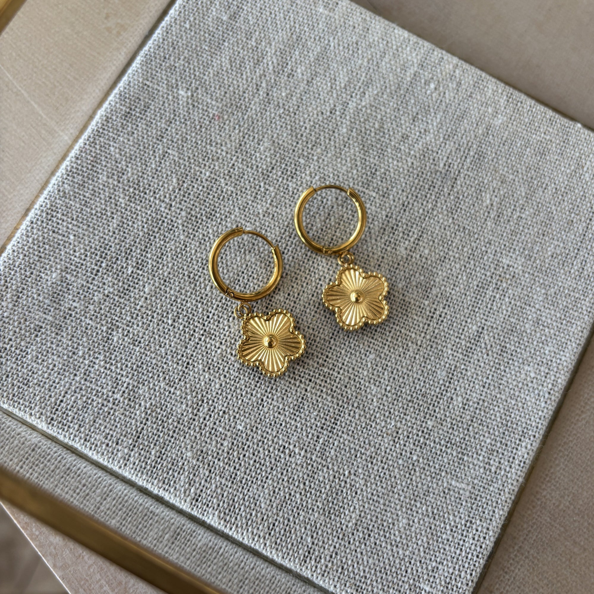 Gold hoop earrings with floral charms on a textured gray surface