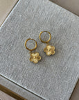 Gold hoop earrings with floral charms on a textured gray surface