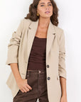Woman wearing a beige blazer over a brown top and pants on a white background