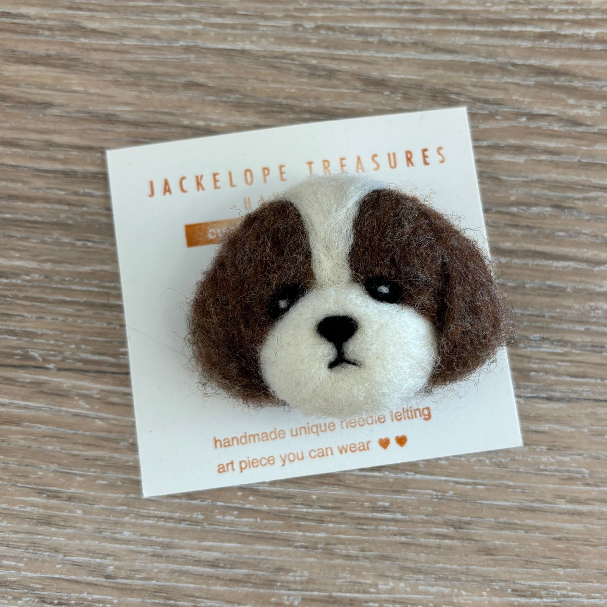 Felted animal head pin on a card with 'Jackelope Treasures' branding on a wooden surface.