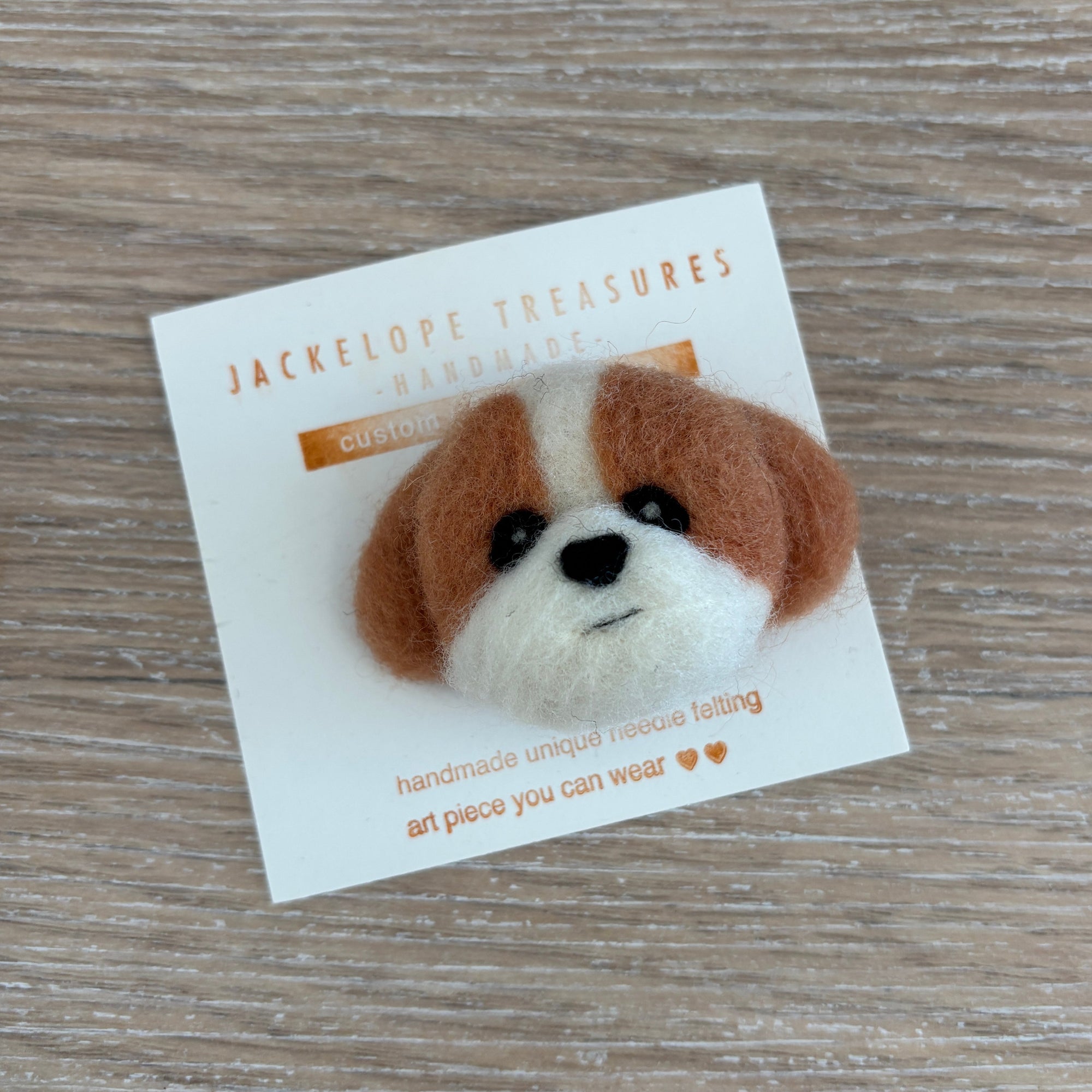 Felted dog head pin on a card with 'Jackelope Treasures' branding on a wooden surface.