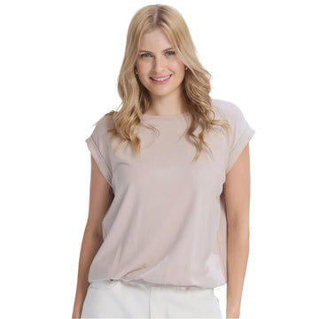 Woman wearing a beige top and white pants against a plain background