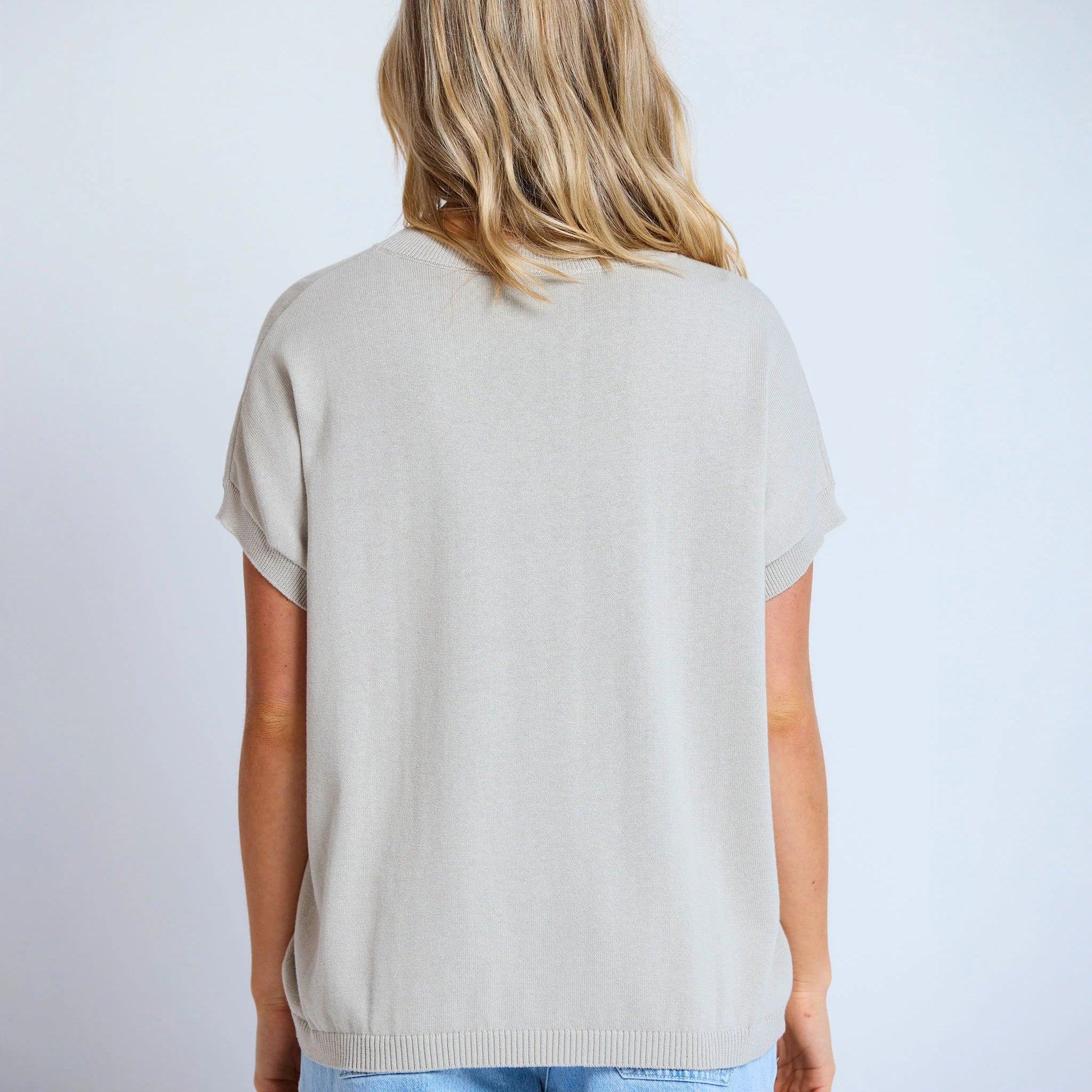 Person wearing a beige t-shirt and light blue jeans on a plain background