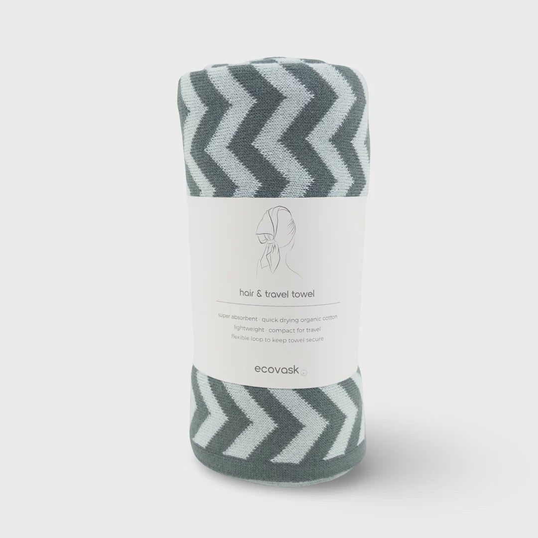 A rolled-up gray and white chevron-patterned travel towel with a white paper label wrapped around it, photographed on a light gray background.