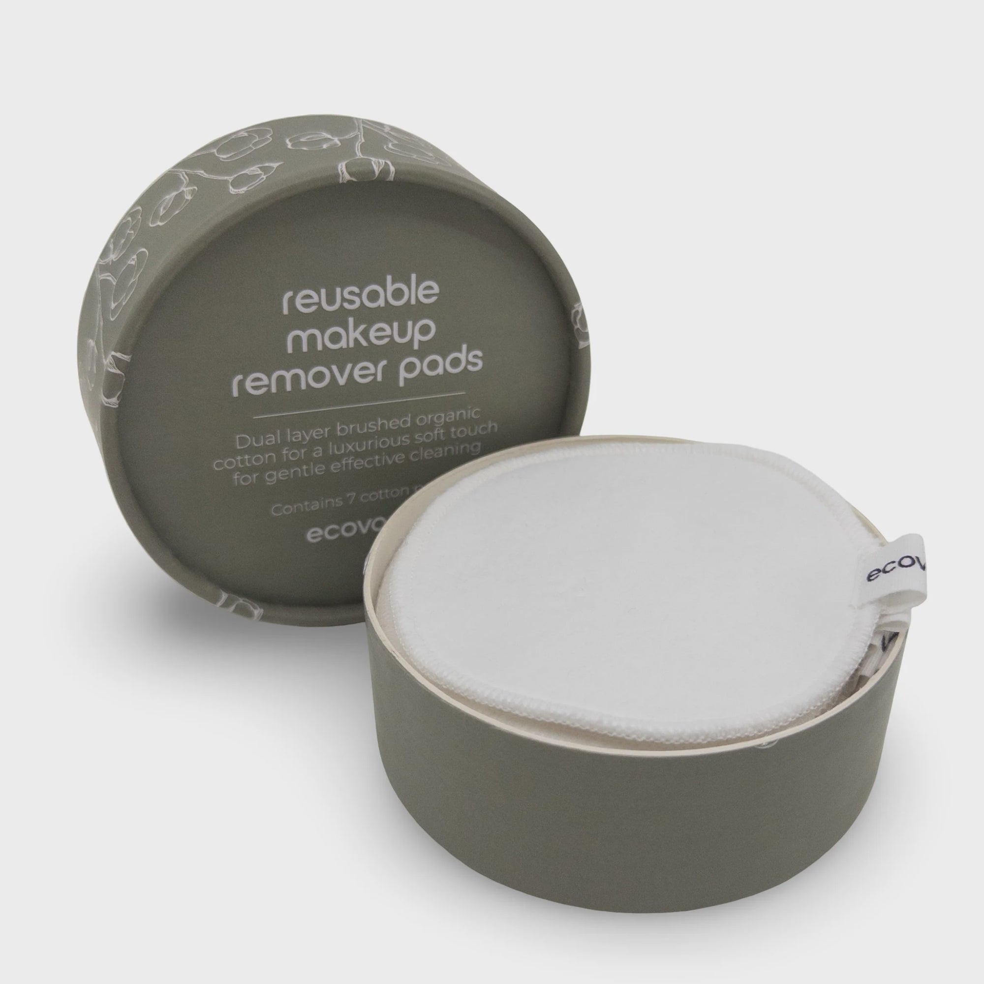 A reusable makeup remover pad in a round matte olive-green container, shown open with the white cotton pad inside. The matching lid sits behind it on a clean light gray background.