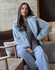 Woman wearing a light blue coat sitting on a couch in a modern interior setting