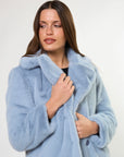 Woman wearing a light blue fur coat against a white background