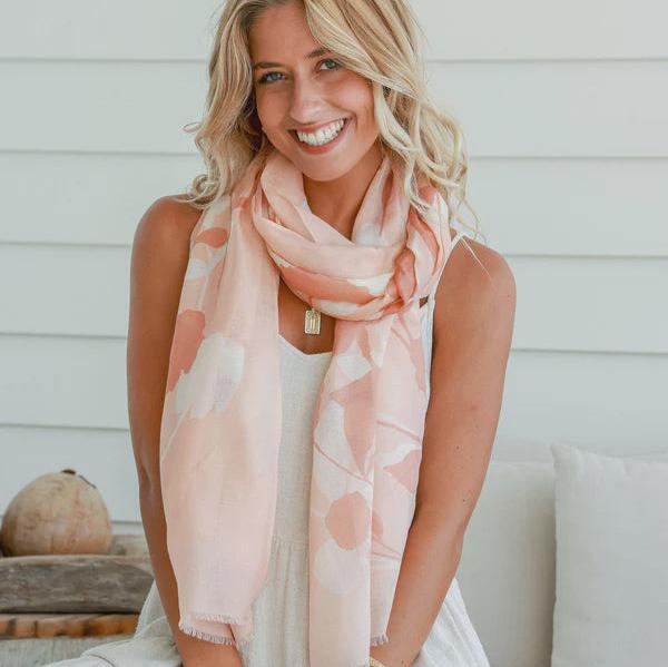 Woman wearing a light pink floral scarf with a neutral background