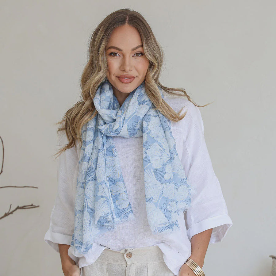 Woman wearing a light blue floral scarf with a plain background